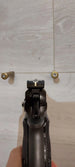Black handgun with textured grip and rear sight, held against light wood background with two brass cartridges.