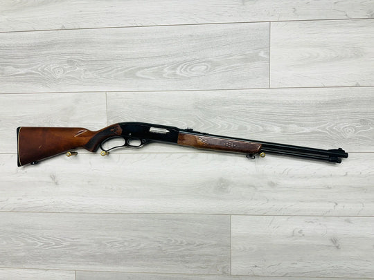 Classic wooden-stocked shotgun with ornate grip, ideal for hunting or collection, displayed on light wood floor.