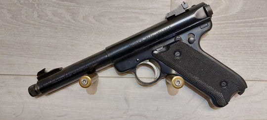 Ruger .22 Cal Long Rifle pistol with textured grip, displayed on wood surface with two cartridges