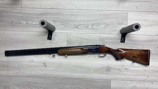 Used hunting shotgun with wooden stock and barrel protectors on gray floor, ideal for sport shooting.