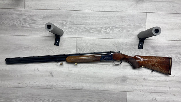 Used hunting shotgun with wooden stock and barrel protectors on gray floor, ideal for sport shooting.
