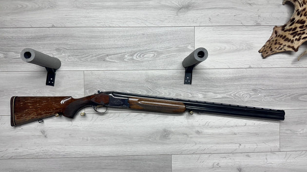 Used hunting shotgun with wooden stock, barrel protectors, and ammo on wood floor, ideal for collectors or sport shooting.