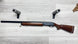 Mossberg Model 1000 shotgun with wood stock, displayed on light wood floor with foam barrel supports