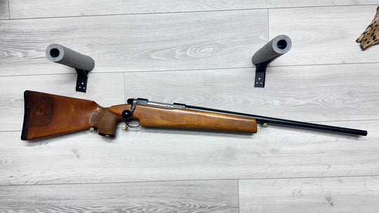 Wooden stock hunting rifle with foam gun rests on light wood floor, ideal for sport shooting or collection
