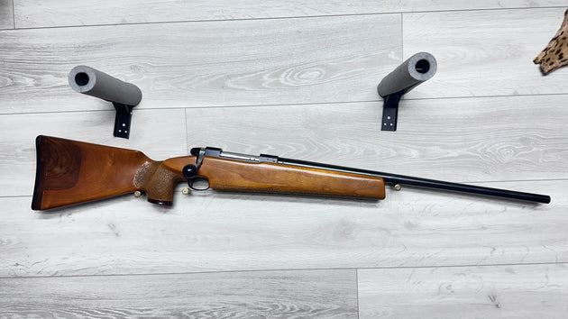 Wooden stock hunting rifle with foam gun rests on light wood floor, ideal for sport shooting or collection