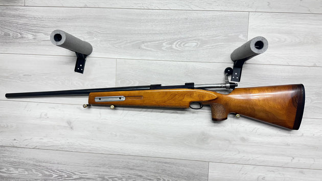 Wooden stock rifle with foam rests on light wood floor, ideal for hunting or sport shooting