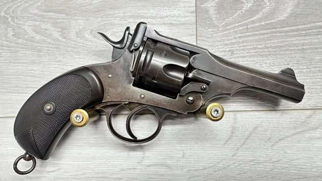 Vintage revolver with textured grip and brass cartridges, displayed on wood surface for collectors