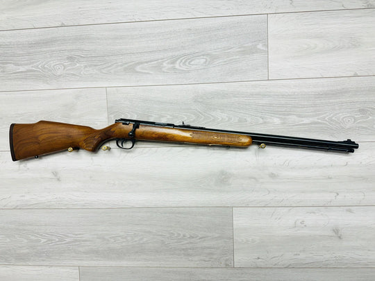 Wooden stock rifle with engraved details, ideal for hunting or sport shooting, displayed on light wood floor.