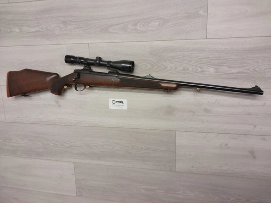 Wooden stock rifle with scope for hunting or sport shooting, displayed on light wood floor