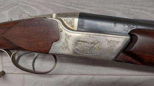 Elegant engraved shotgun with detailed wildlife scene, wooden stock, and ornate metalwork for hunting or collection.