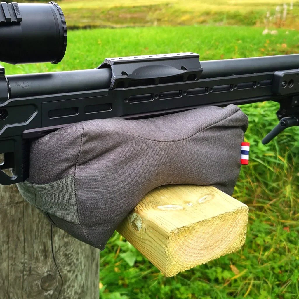 Rifle with scope resting on shooting bag and wooden block outdoors, ideal for precision shooting and hunting.
