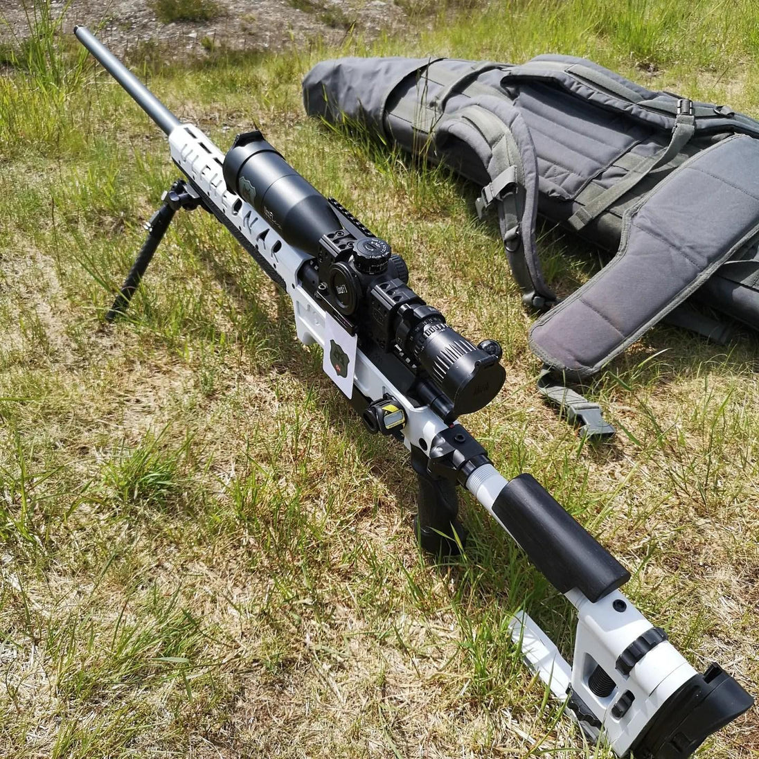 White tactical rifle with scope and bipod on grass, ideal for precision shooting and hunting