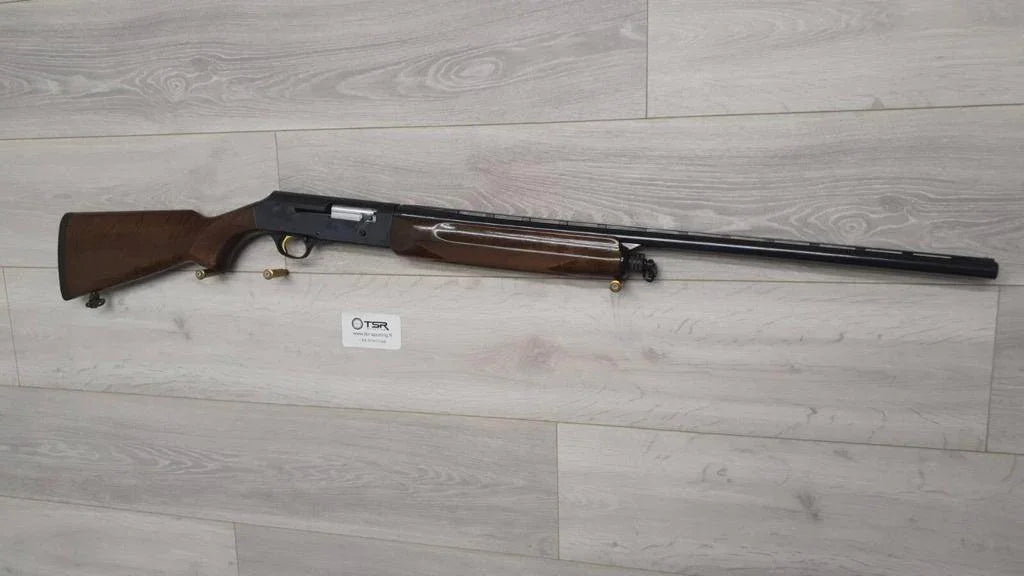 Used hunting shotgun with wooden stock, displayed for sale on light wood floor