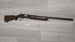 Used hunting shotgun with wooden stock, displayed for sale on light wood floor