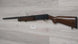 Used hunting shotgun with wooden stock displayed on wall, ideal for sport shooting and collection