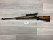 Wooden stock rifle with scope for hunting or sport shooting, displayed on gray wood floor
