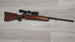 Wooden stock rifle with scope, ideal for hunting or sport shooting, displayed on light wood floor.