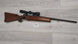 Wooden stock rifle with scope, ideal for hunting or sport shooting, displayed on light wood floor.