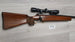 Wooden stock rifle with scope, ideal for hunting and target shooting, displayed on light wood floor.