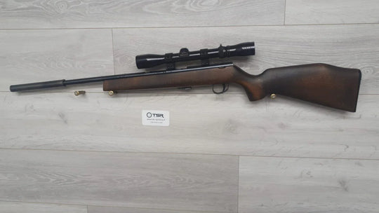 Wooden stock rifle with scope, ideal for hunting and sport shooting, displayed on light wood floor.