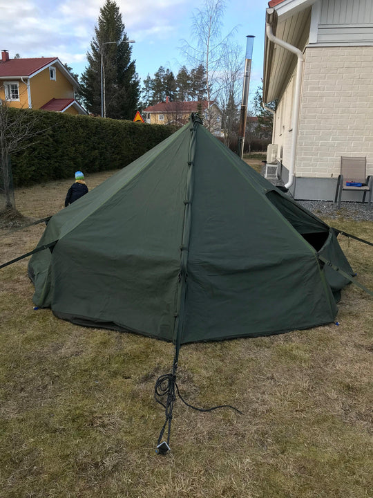 Green military-style pyramid tent set up in backyard, ideal for camping or outdoor survival gear.
