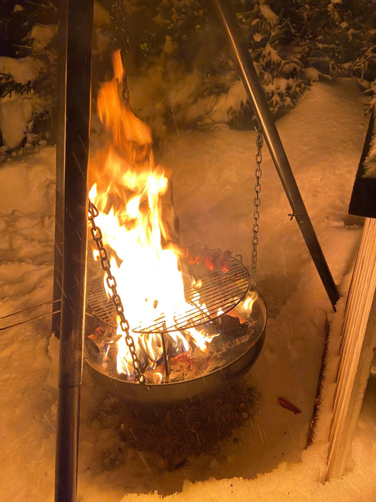 Outdoor fire pit grill roasting sausages in snow, perfect for winter camping or backyard gatherings.