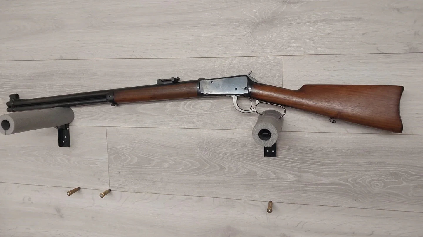 Vintage lever-action rifle with wooden stock displayed on wall mount, ideal for collectors and hunting enthusiasts.