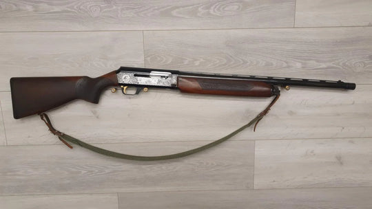 Elegant hunting shotgun with engraved receiver, wooden stock, and green sling on light wood floor