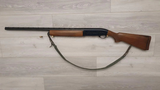 Wooden stock shotgun with sling, ideal for hunting or sport shooting, displayed on light wood floor.