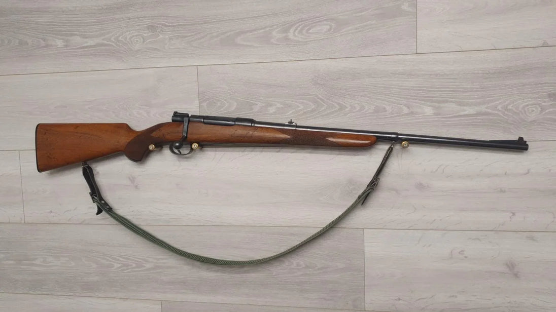 Wooden-stocked hunting rifle with sling on light wood floor, ideal for collectors and sport shooting.