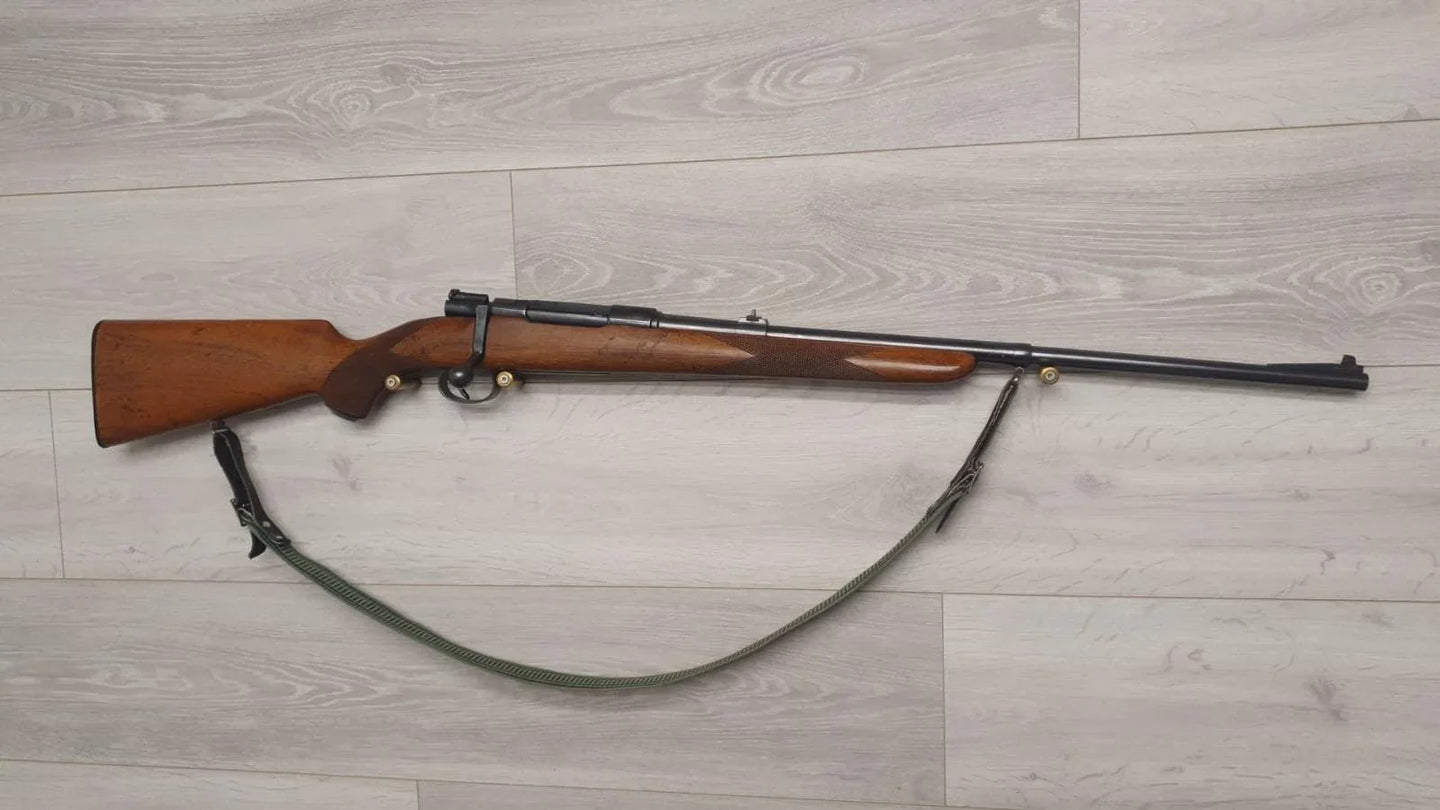 Wooden-stocked hunting rifle with sling on light wood floor, ideal for collectors and sport shooting.