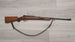 Wooden-stocked hunting rifle with sling on light wood floor, ideal for collectors and sport shooting.