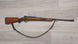 Wooden-stocked hunting rifle with sling on light wood floor, ideal for collectors and sport shooting.