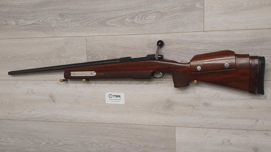 Wooden stock bolt-action rifle for hunting or sport shooting, displayed on light wood floor