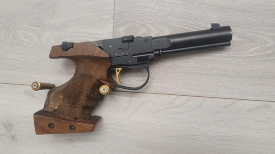 Morini 102 E .22 LR competition pistol with wooden grip, gold trigger, and .22 ammo on light wood floor